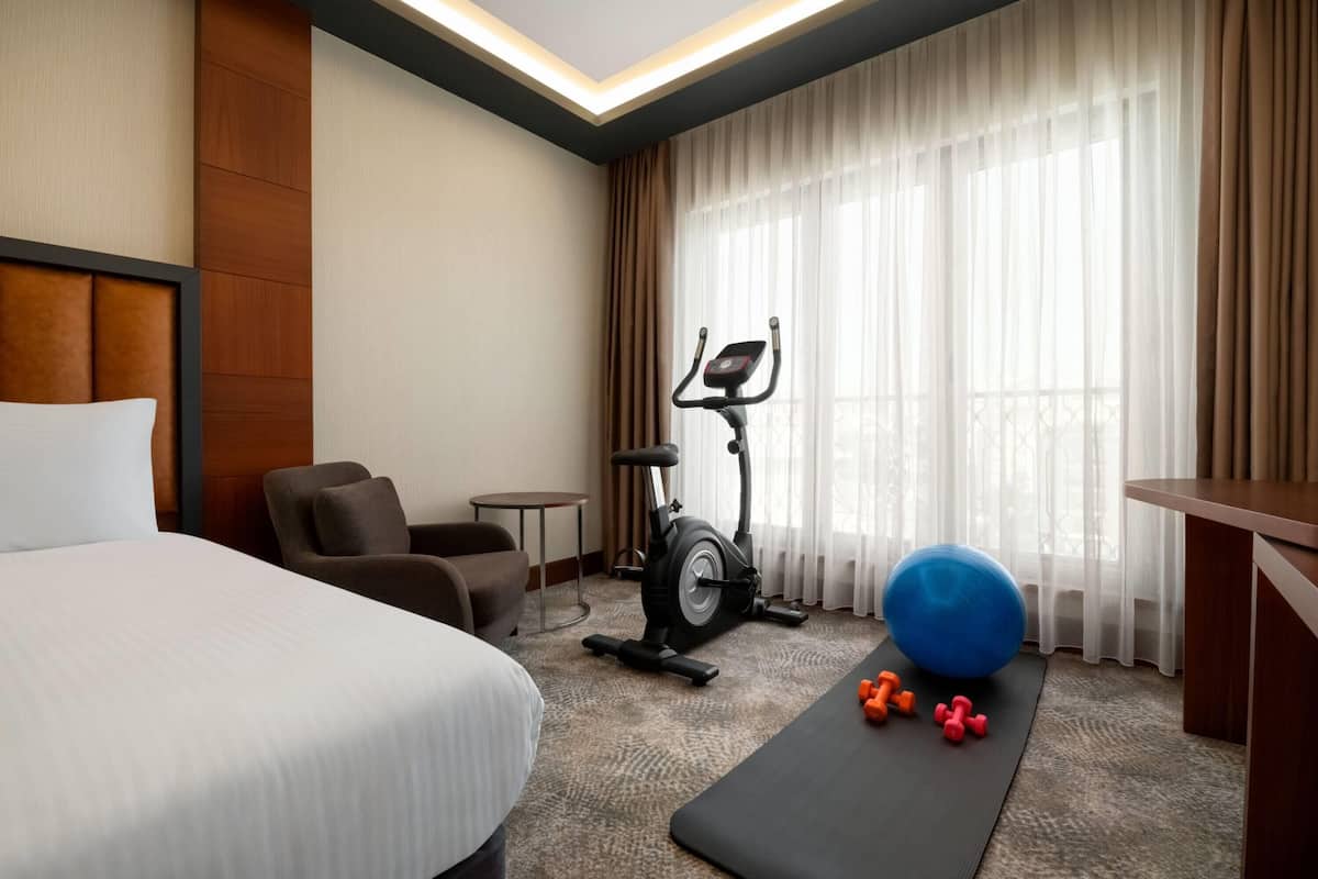 A hotel room with a bed, exercise equipment, a small table, and a window with curtains.