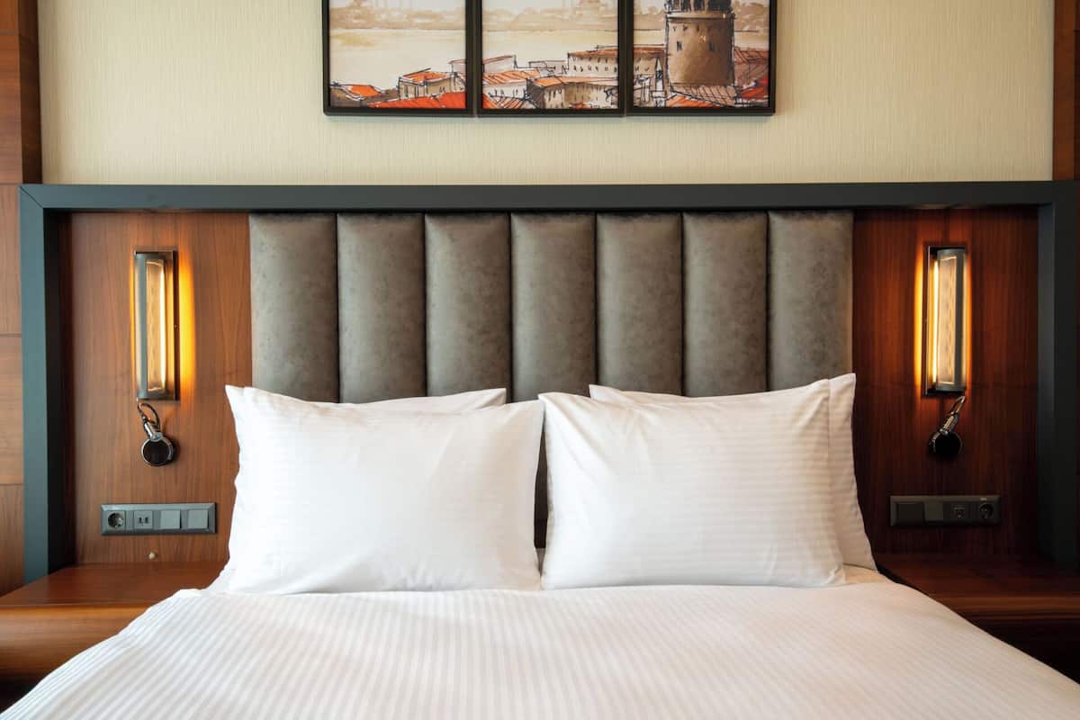 A hotel room with a large bed, two wall-mounted lamps, and a cityscape painting above the bed.