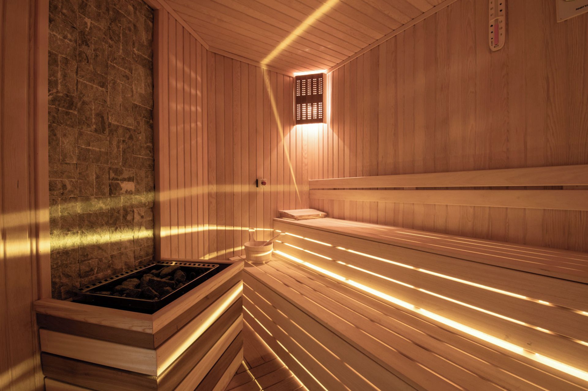 A sauna with wooden benches, a stone wall, and a small window.