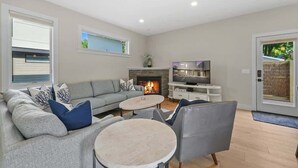 Una sala de estar moderna con un sofá gris, dos mesas redondas de centro, una chimenea y un televisor.