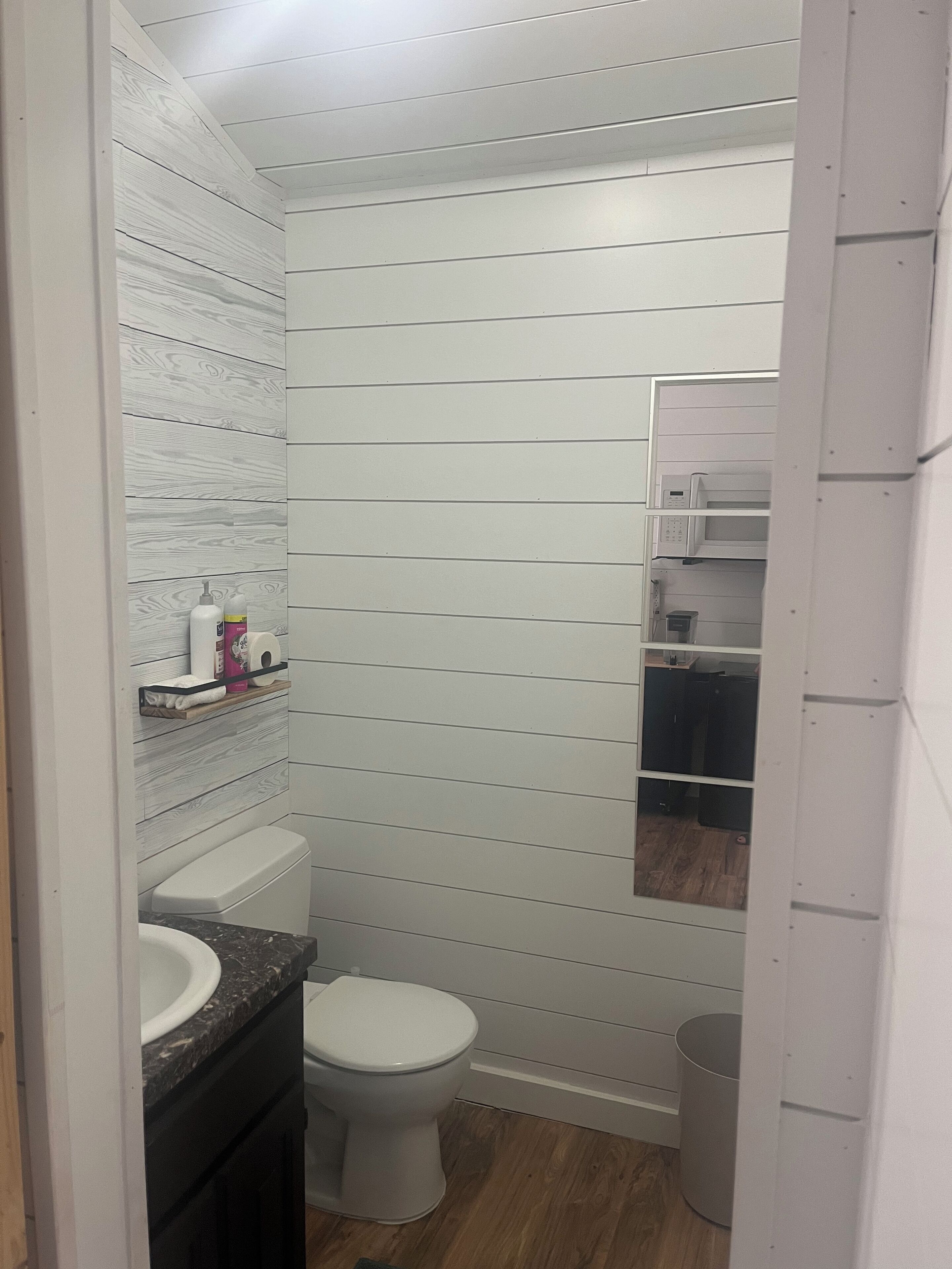 Et badeværelse med et hvidt toilet, en vask med marmorbordplade og et spejl over vasken.