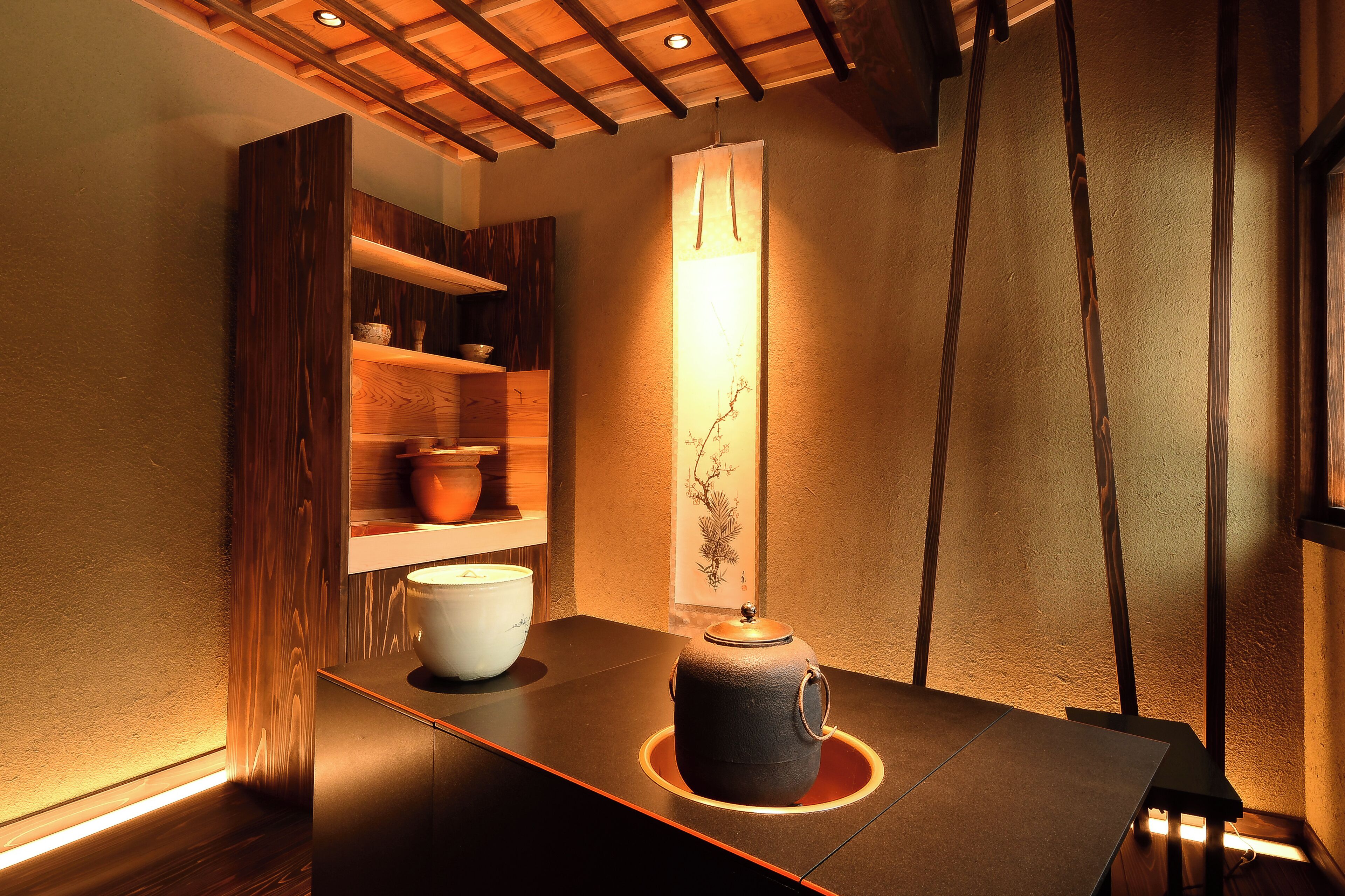 A traditional Japanese-style room with a tatami mat floor, a low table with a tea set, and a wall-mounted shelf with decorative items.