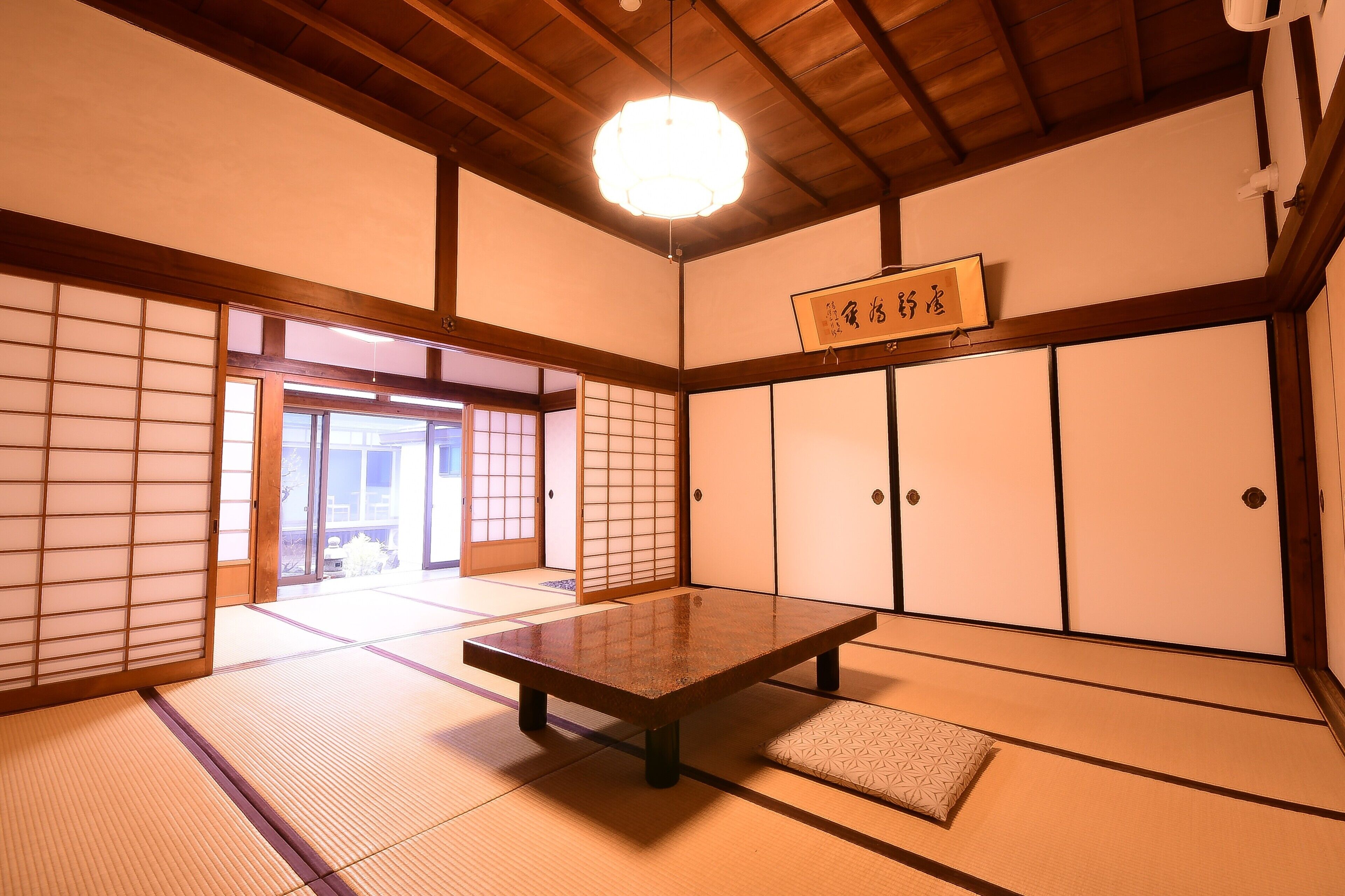 A traditional Japanese room with tatami flooring, a low table, sliding doors, and a hanging sign.