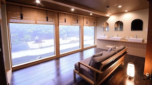 Una habitación moderna con ventanas amplias, un sofá, un banco de madera y un baño con dos lavamanos.