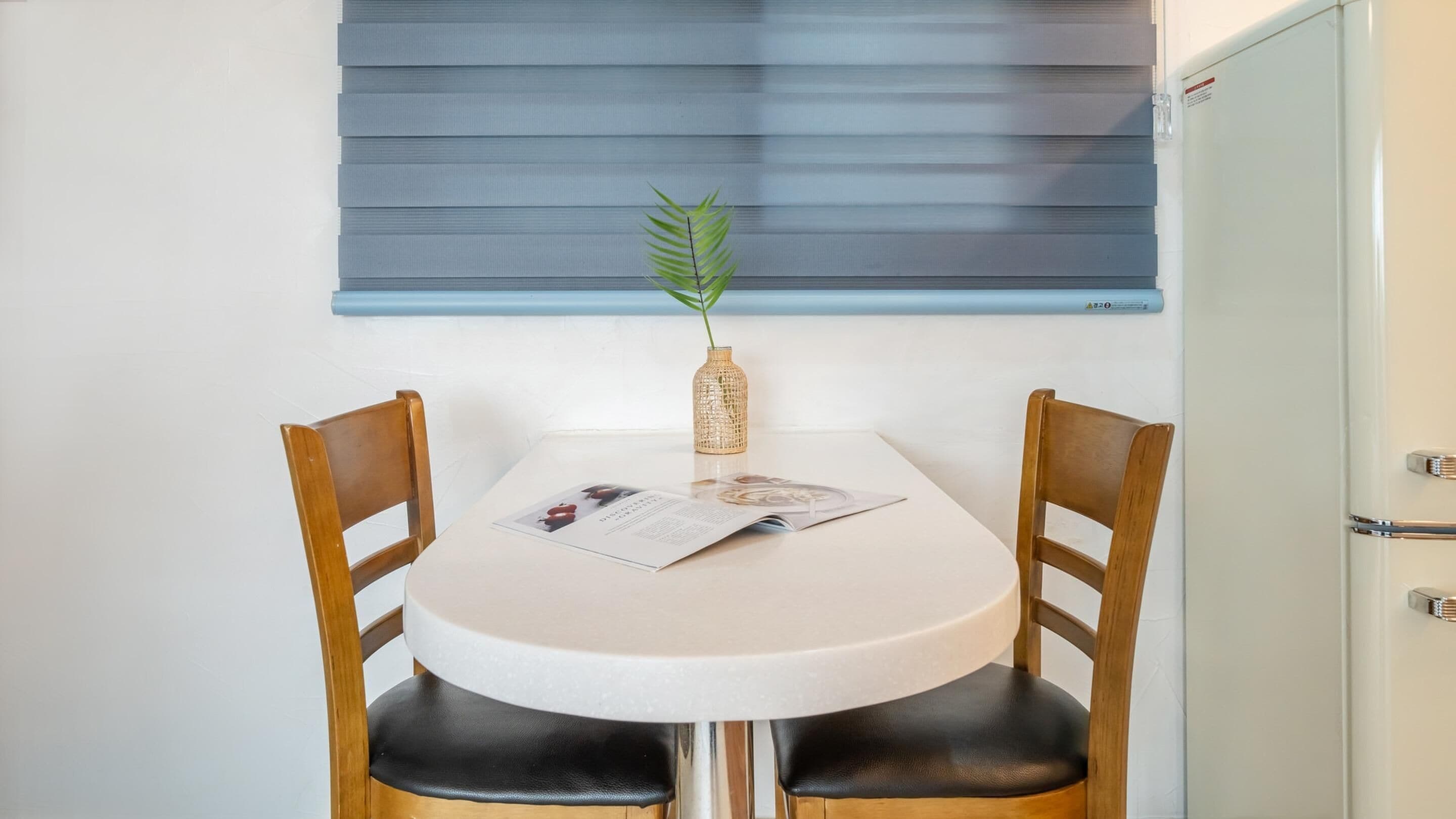 Een kleine eettafel met twee houten stoelen, een enkele glazen vaas met een plantje, en een menukaart op de tafel.