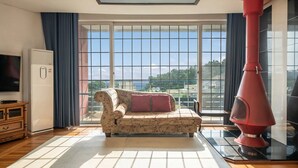 A living room with a sofa, a red fireplace, a television, and large windows with a view. - Ganghwado Happyvilly Pension (Incheon)