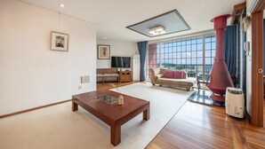 A spacious living room with a wooden coffee table, a sofa, and a large window offering a view of the outdoors. - Ganghwado Happyvilly Pension (Incheon)
