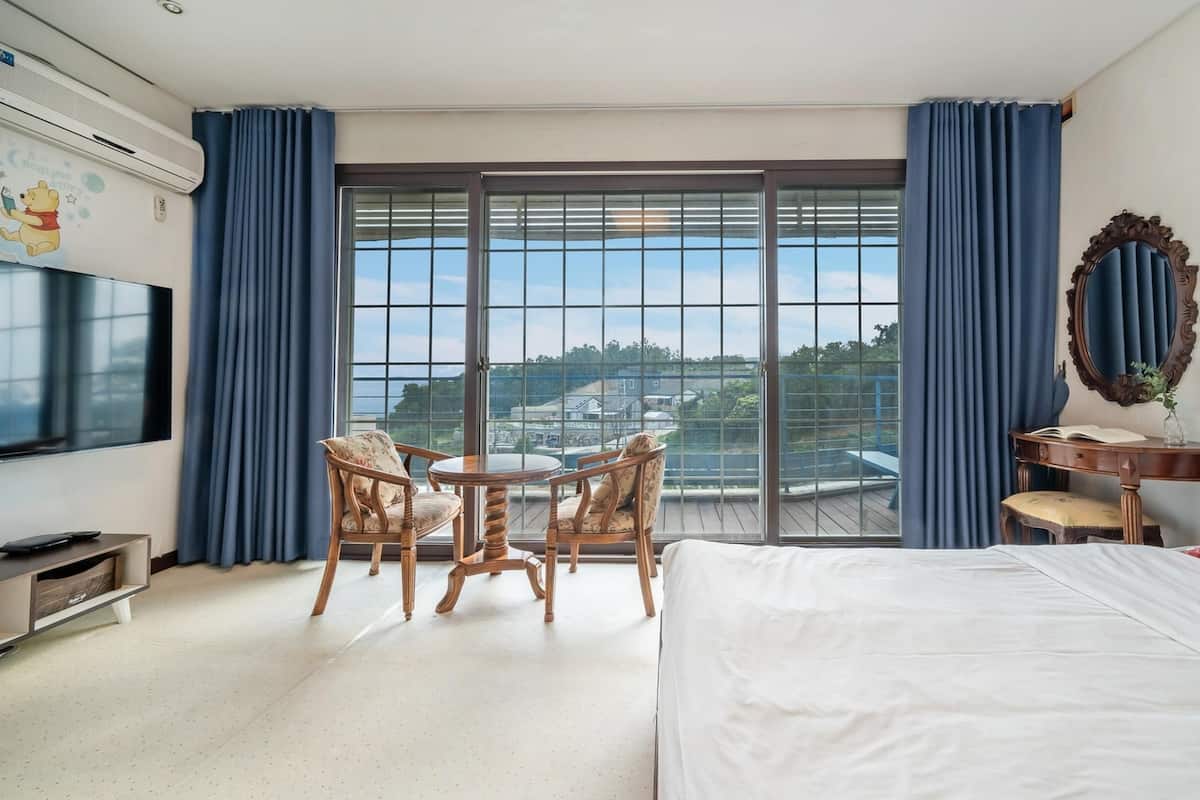 Une chambre d’hôtel avec un grand lit, un bureau avec une chaise, une télévision et une vue sur la ville grâce à de grandes fenêtres.