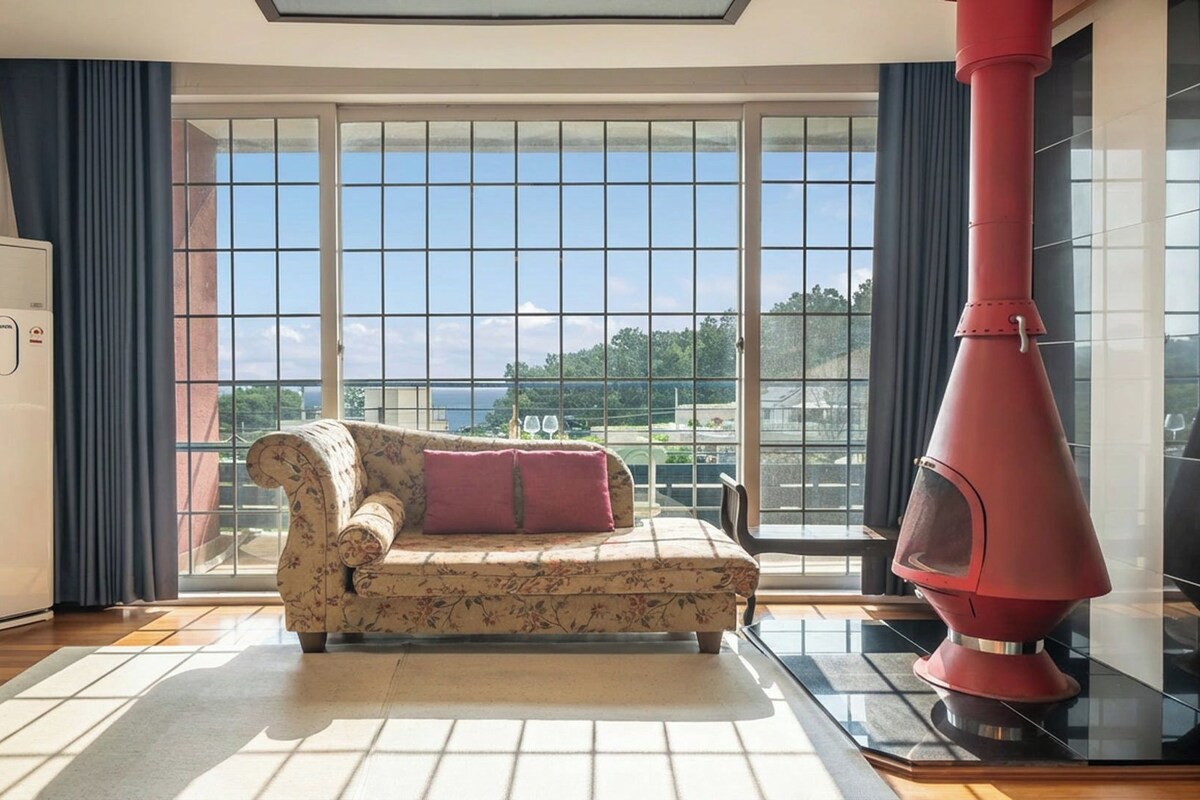 A living room with a sofa, a television, a fireplace, and a large window with a view.