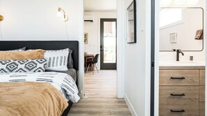 Une chambre à coucher moderne, avec un lit, une table de chevet et une salle de bain équipée d’un miroir et d’un lavabo.