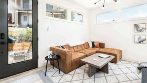 Un salon moderne avec un canapé d’angle, une table basse et une grande fenêtre offrant une vue sur l’extérieur.