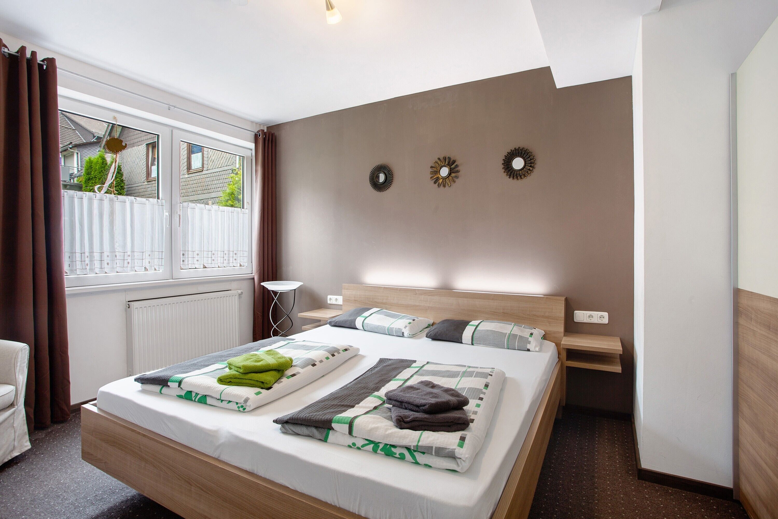 A modern hotel room with a large bed, a bedside table, a nightstand, and a view of the outside.