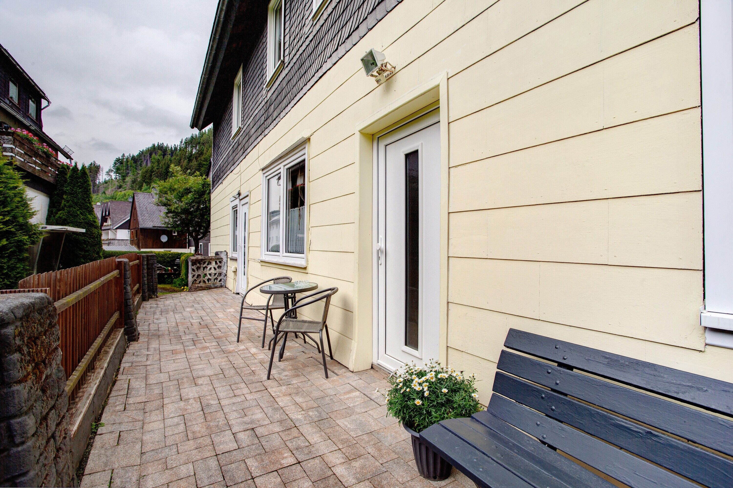 A paved patio with a wooden bench and a small table with chairs.