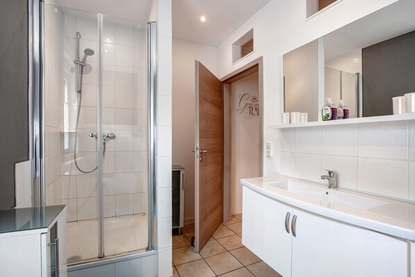 A modern bathroom with a glass-enclosed shower, a white sink, and a mirror above the countertop.