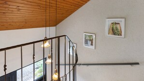 Een houten plafond, een trap met een metalen leuning, en twee ingelijste foto's aan de muur.