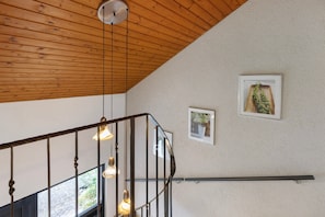 Een houten plafond, een trap met een metalen leuning, en twee ingelijste foto's aan de muur.