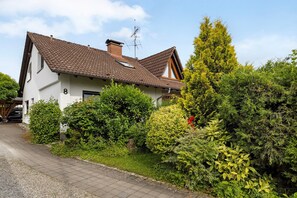 Une maison à deux étages, avec un toit recouvert de tuiles, une cheminée et une antenne parabolique bien visible.