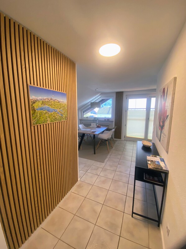 Ein Zimmer mit einem Esstisch, Stühlen, einem schwarzen Beistelltisch mit Zeitschriften, einem Heizkörper und einem Fenster mit Jalousien.