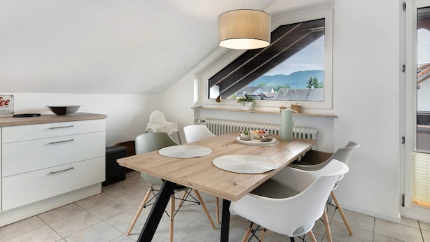 Een moderne keuken met een houten tafel, witte stoelen, een hanglamp en een raam met uitzicht op bergen.