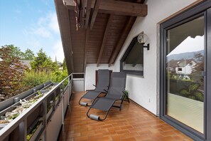 A balcony with two lounge chairs, a window, and a view of greenery and buildings.