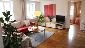 Ein Wohnzimmer mit einer Couch, einem Couchtisch, einem Fernseher und Topfpflanzen.