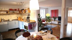 Eine moderne Küche mit weißen Schränken, ein Essbereich mit einem runden Tisch und ein Wohnzimmer mit Fernseher.