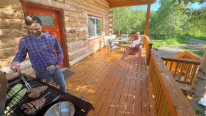 A wooden cabin with a deck, a grill, and a dining area. - Riverfront, Authentic, Luxury Log Cabin-Bison (Wasilla)