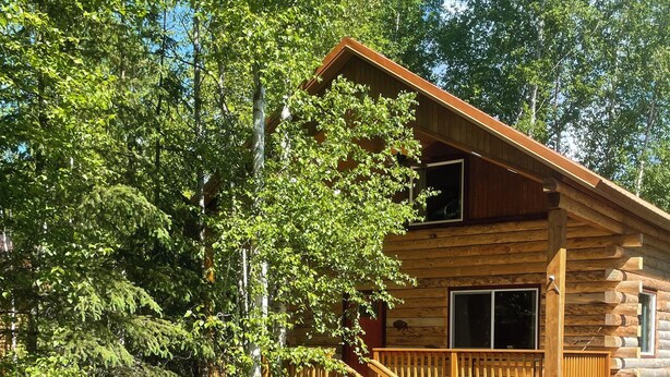 A wooden cabin with a balcony and stairs, surrounded by trees. - Riverfront, Authentic, Luxury Log Cabin-Bison (Wasilla)