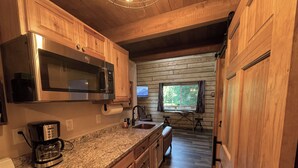 A kitchen with wooden cabinets, a stainless steel microwave, a coffee maker, and a window with a view of the outdoors. - Riverfront, Authentic, Luxury Log Cabin-Bison (Wasilla)