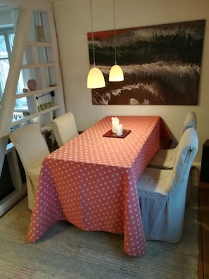 Un comedor con una mesa cubierta por un mantel rojo, dos sillas, un cuadro en la pared y una escalera apoyada contra la pared.