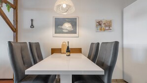 A dining area with a white table, black leather chairs, a bottle of wine, a framed artwork, and a wall-mounted light fixture.