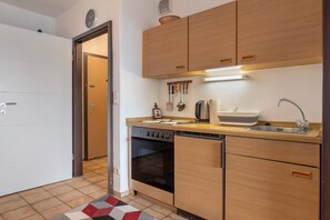 Una cocina compacta con armarios de madera, horno empotrado, lavavajillas y pileta.