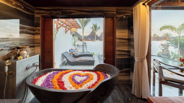 Une salle de bain moderne dotée d’une grande baignoire, d’une douche et offrant une vue sur une piscine et des palmiers.