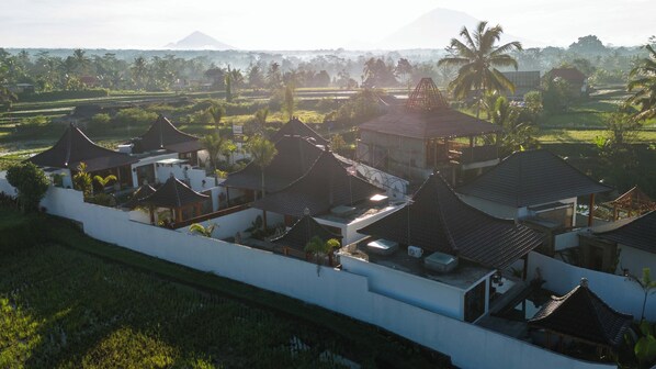A residential area with traditional-style houses, a white wall, and a view of a mountain in the background. - Maddu Suites (Sebatu)