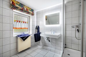 Une salle de bain moderne équipée d’une douche, d’un lavabo et d’une fenêtre avec des rideaux.