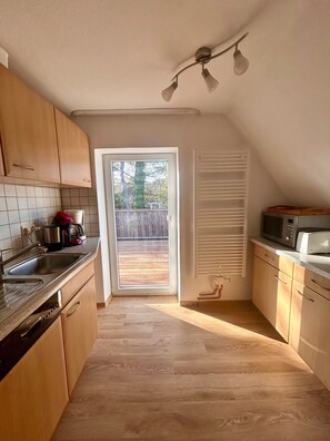 A kitchen with wooden cabinets, a stainless steel sink, a microwave, and a sliding glass door leading to an outdoor area. - Holiday Home 'Haus Seeluft' with Private Terrace, Shared Garden and Wi-Fi (Sankt Peter-Ording)