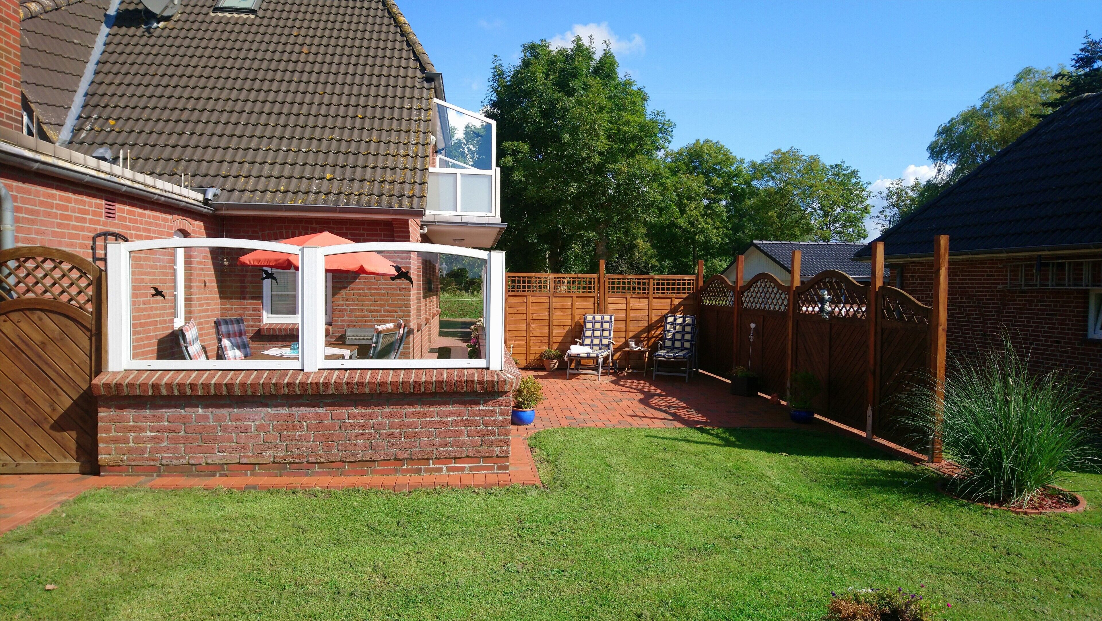 Een bakstenen huis met een terras, een houten omheining en een tuin.