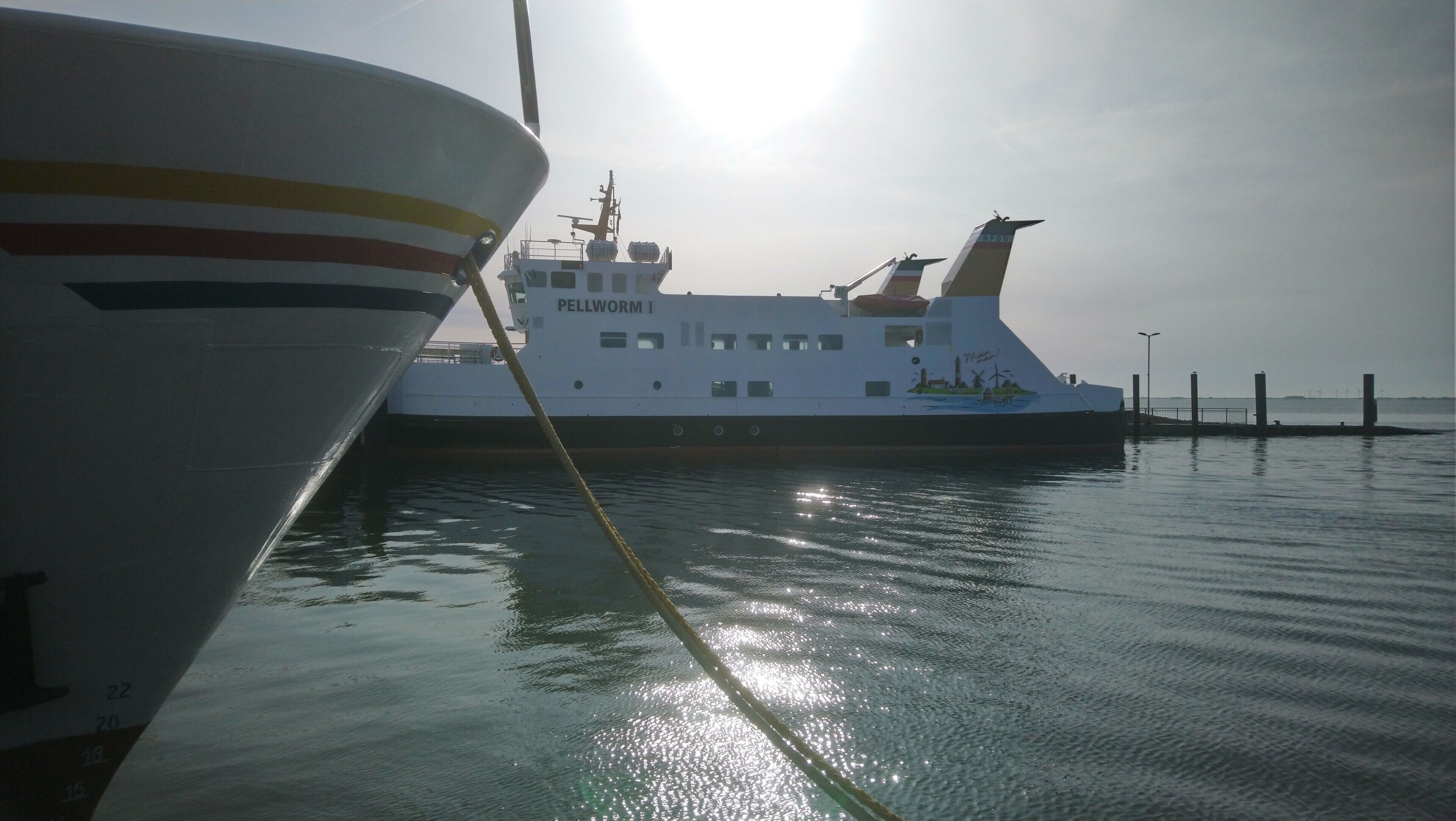 A ferry docked at a pier with a clear view of the water and the sun shining.