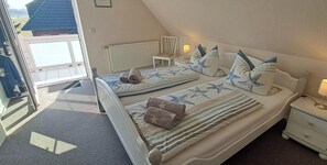 Ein Schlafzimmer mit zwei Betten, Blick ins Freie, einem Sessel, einem Nachttisch und einer Lampe.