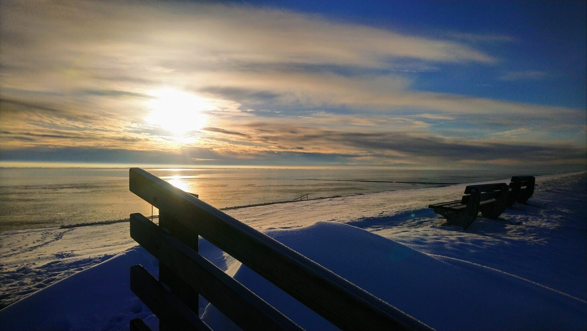 A bench overlooking a frozen body of water with the sun low on the horizon.
