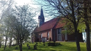 A church with a tall steeple, a brick building, and a cemetery with headstones. - Apartment 'Michelsen' with Private Terrace, Private Garden and Wi-Fi (Nordstrand)