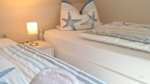 A hotel room with a bed, a nightstand with a lamp, and star-patterned pillows. - Apartment 'Michelsen' with Private Terrace, Private Garden and Wi-Fi (Nordstrand)