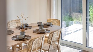 Une table à manger entourée de chaises en osier, une fenêtre en verre et une vue sur la verdure à l’extérieur.