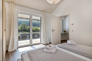 A bedroom with two beds, a balcony with a view of trees, and a sliding glass door.