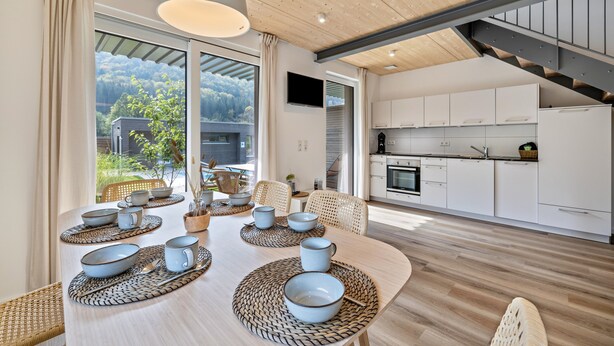 Une cuisine moderne avec des armoires blanches, un four encastré et un coin repas avec une table dressée pour quatre personnes.