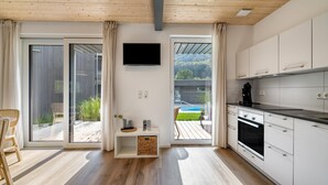 Une cuisine moderne avec des meubles blancs, un téléviseur à écran plat et une porte-fenêtre coulissante donnant sur une terrasse extérieure.