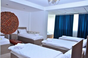 A hotel room with four single beds, a large decorative wall hanging, and a view of the outside through blue curtains. - Karvan-N (Tashkent)