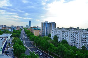 A cityscape with a multi-lane road, high-rise buildings, and green trees lining the street. - Karvan-N (Tashkent)