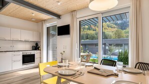 A modern kitchen with white cabinets, a dining area with yellow chairs, and a large window with a view of trees and a pool.