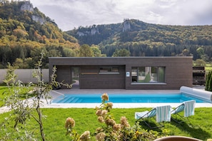 A modern house with a swimming pool, a grassy yard, and a mountain backdrop.